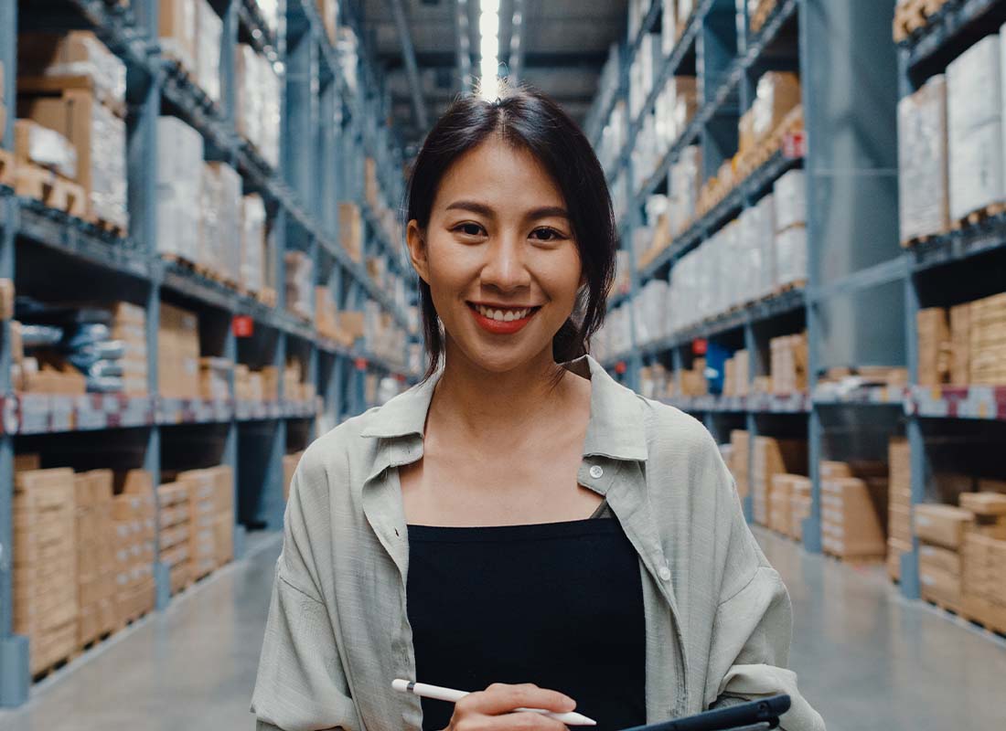 Workers’ Compensation Insurance - Portrait of Young Business Manager Smiling and Looking at Camera While Holding a Tablet and Standing in Retail Distribution Center