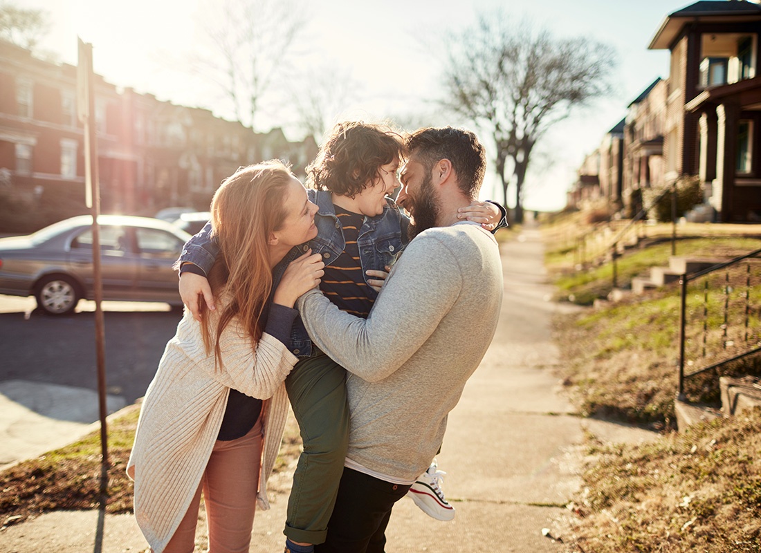 Personal Insurance - Portrait of Parents Hugging Their Young Son Outside in a Small Neighborhood in the City at Sunset While Walking on the Sidewalk