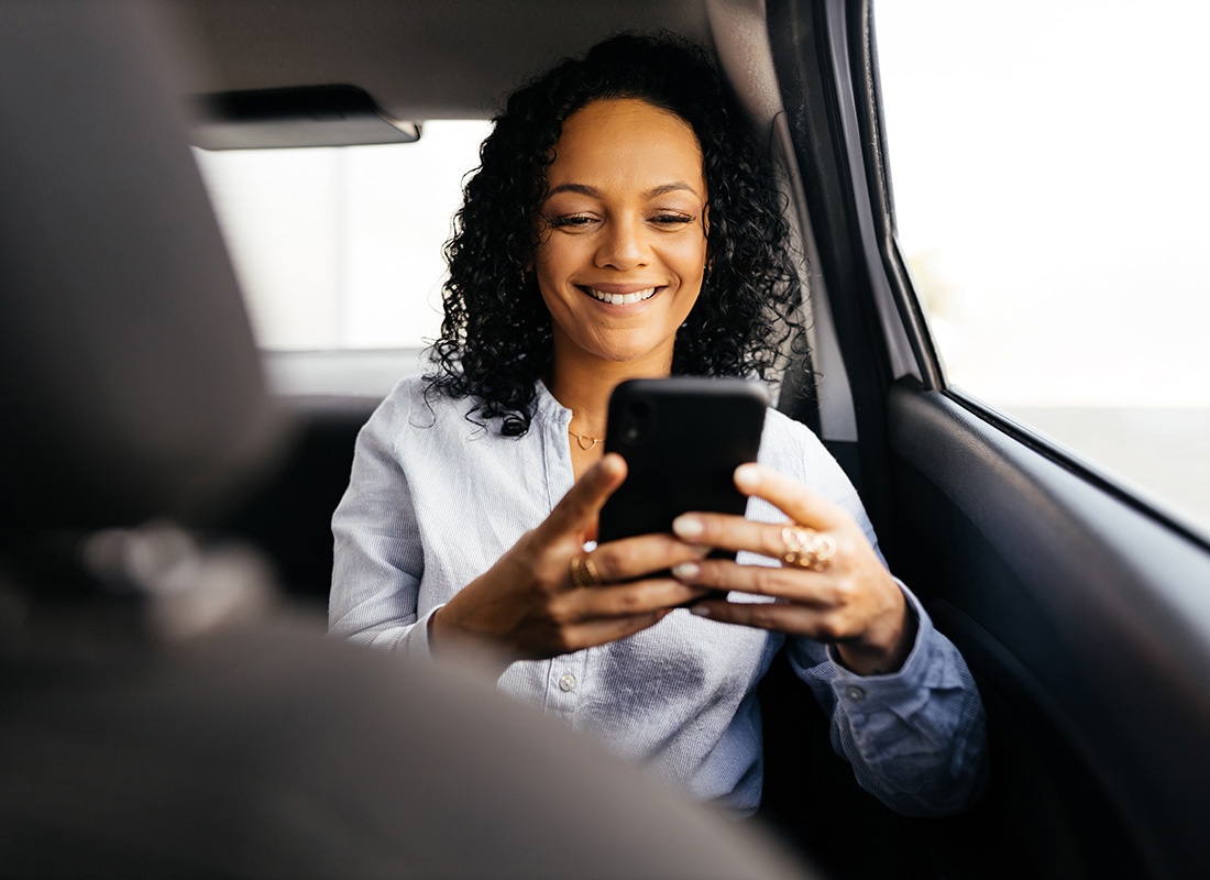 Service Center - Portrait of a Cheerful Young Business Woman Sitting in the Back Seat of a Car While Using a Phone
